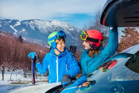 Photo for Happy mother and young boy stand near car looking at each other as they arrived on winter vacation alpine destination to ski or snowboard - Royalty Free Image