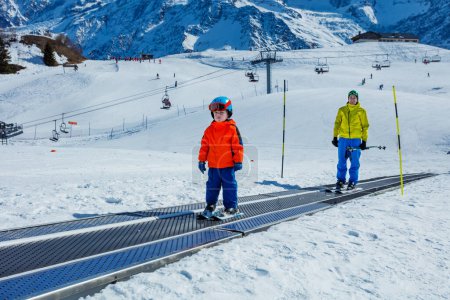 Photo for Little boy and a father go up on the ski moving walkway belt at skiing school during winter vacations - Royalty Free Image