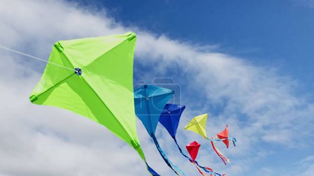 Téléchargez les photos : Group of many beautiful colorful kites fly on the string over blue sky with clouds - en image libre de droit