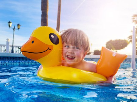 Photo for Laughing cute boy in buoy and floaties having fun swimming splashing in the sunset pool - Royalty Free Image
