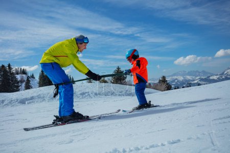 Foto de Instructor en la escuela de esquí se desliza hacia atrás enseñando a los niños a esquiar yendo cuesta abajo sosteniendo los postes juntos - Imagen libre de derechos