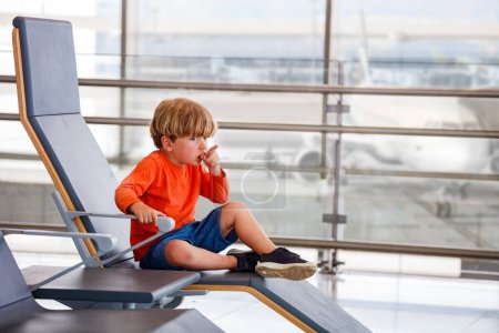 Foto de Niño espera a que el vuelo se siente en la silla en el aeropuerto se abalanza mirando aviones señalando el dedo - Imagen libre de derechos