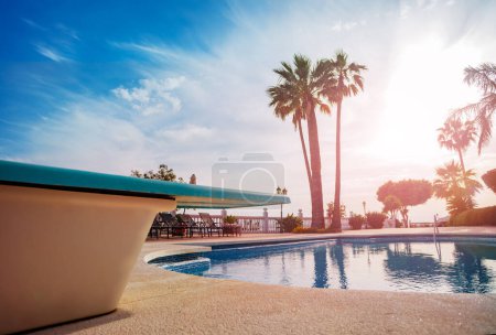 Foto de Primer plano de un trampolín sobre la piscina abierta durante el atardecer a través de palmeras del sur en la calurosa noche de verano - Imagen libre de derechos