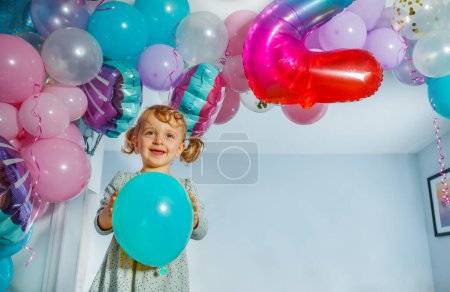 Foto de Niña de pie celebración fiesta globo sobre decoraciones en el cumpleaños del niño en casa - Imagen libre de derechos