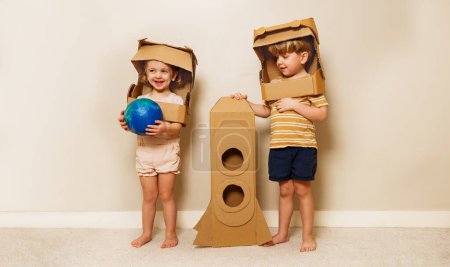 Foto de Happy kids sister and brother stand with cardboard rocket in astronauts DIY helmets holding planet earth - Imagen libre de derechos