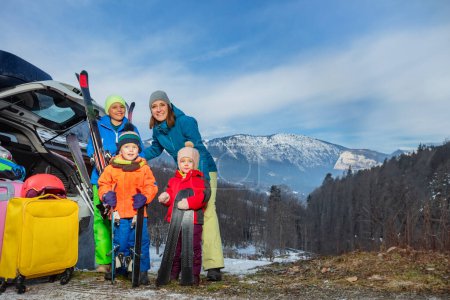 Photo for Mom stand holding ski by open car trunk arrived with 3 kids at alpine skiing resort unloading suitcases and baggage - Royalty Free Image