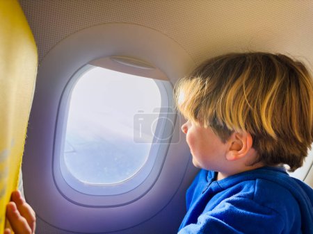 Foto de Lindo niño pequeño sentarse y mirar la ventana en el avión mirando porthole durante el primer vuelo - Imagen libre de derechos