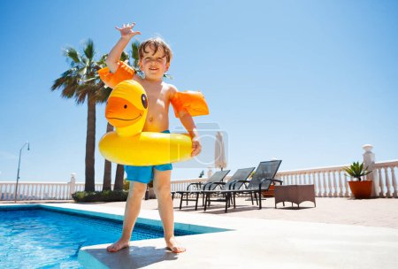 Photo for Cute boy waving hands standing on the edge of the pool ready to dive in clear blue water - Royalty Free Image