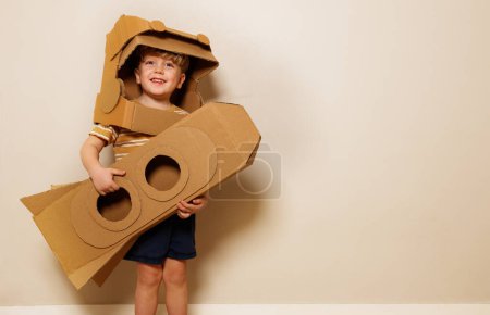 Foto de Alegre joven usa un casco de cartón mientras sostiene su cohete casero mientras imaginaba viajar a través de los misterios del espacio exterior - Imagen libre de derechos