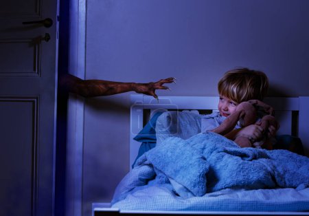 Foto de Mano del monstruo con garras tratando de alcanzar al niño en la cama sosteniendo un juguete de peluche pero sin miedo - Imagen libre de derechos