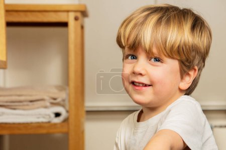 Téléchargez les photos : Beau garçon blond heureux dans la salle de bain souriant avec expression calme - en image libre de droit