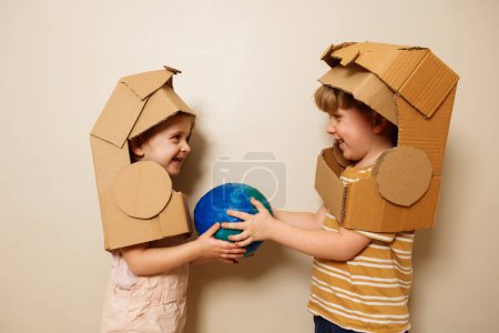 Foto de Dos hermosos niños en astronauta de cartón casco de juguete hermoso planeta planeta planeta tierra globo modelo y sonriendo - Imagen libre de derechos