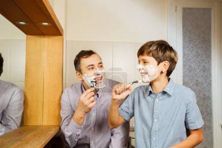 Photo for Father and kid holding razor smiling at each other shaving faces covered with shave foam in bathroom - Royalty Free Image