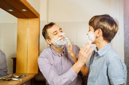 Téléchargez les photos : Papa et son adolescent s'amusent dans la salle de bain à raser en mettant de la mousse à raser sur le visage de l'autre - en image libre de droit