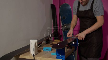 Photo for Man service ski taking out excessive wax with plastic tool at the workshop holding skies in vice - Royalty Free Image