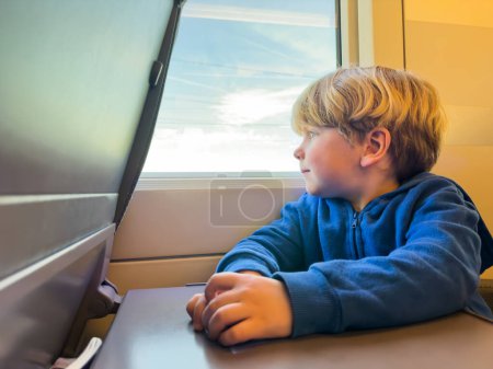 Téléchargez les photos : Petit garçon assis et regardant par la fenêtre dans le train à grande vitesse - en image libre de droit