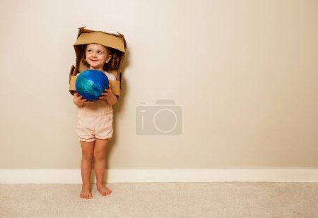 Photo for Beautiful cute girl in cardboard astronaut helmet hold planet earth blue green globe model in hands - Royalty Free Image