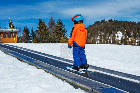 Foto de Niño en el cinturón de la pasarela de esquí en movimiento en la escuela de esquí durante las vacaciones de invierno vista desde atrás - Imagen libre de derechos