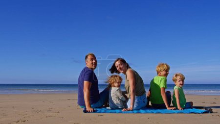 Téléchargez les photos : Famille avec trois enfants mère et père assis sur le partenaire sur la plage de sable ensemble ascenseur revenir en arrière - en image libre de droit