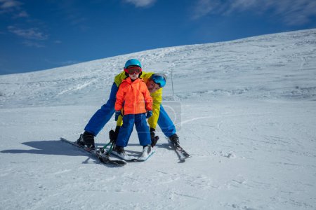 Erwachsener bringt kleinem Kind Skifliegen bei und hält Skibindungen mit Händen, die Schneepflug-Bewegung zeigen