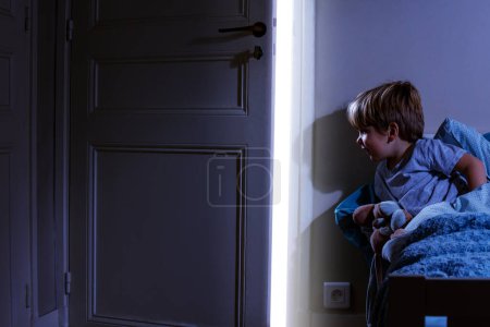 Foto de Lindo chico en el dormitorio mira la luz que viene de la puerta abierta - Imagen libre de derechos