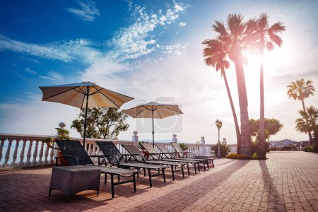 Téléchargez les photos : Fond de vacances avec chaises longues parasols jetant l'ombre près de la piscine et des palmiers sur la lumière chaude du soir - en image libre de droit