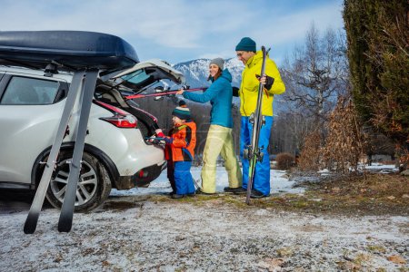 Photo for Family with mom dad and two adorable little kids standing joking unloading ski luggage by the open car trunk - Royalty Free Image