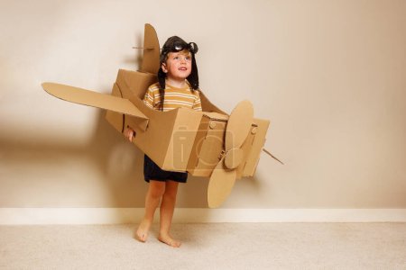Photo for Cute young boy stand holding self made cardboard plane with wings and propeller wearing pilot hat, glasses imagine he flies - Royalty Free Image