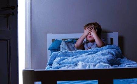 Foto de Niño se sienta en la cama cerrando los ojos - concepto de los niños teme en el dormitorio - Imagen libre de derechos