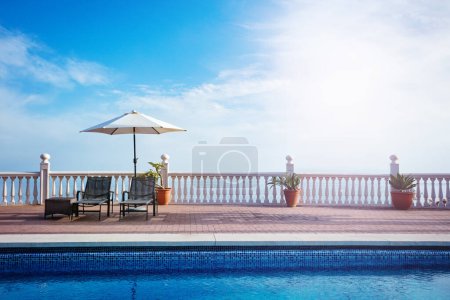 Foto de Piscina con dos de chaise longs sillas de escritorio, sombrilla de playa sombra de fundición sobre el cielo azul - Imagen libre de derechos