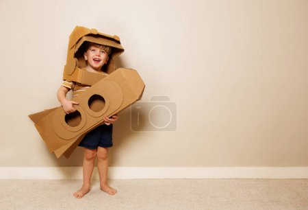 Foto de Feliz chico guapo con su casco de cartón y cohete hecho a sí mismo en las manos sonriente sueño para explorar el espacio - Imagen libre de derechos