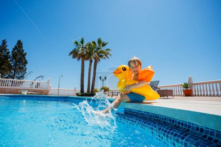 Photo for Boy at resort pool enjoys summer, splashing in buoy and floaties over blue sky - Royalty Free Image
