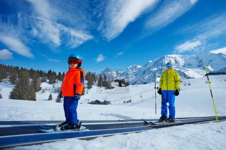 Téléchargez les photos : Petit garçon de 3 ans et un instructeur montent sur la passerelle de ski en mouvement vue sur les sommets de la montagne - en image libre de droit