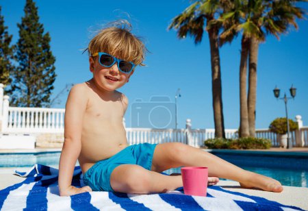Photo for Kid in shades smile on towel by pool in sunny weather enjoy and relax - Royalty Free Image
