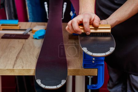 Téléchargez les photos : Gros plan des mains de mans propres, brosse base de ski alpin en atelier pour appliquer un traitement à la cire - en image libre de droit