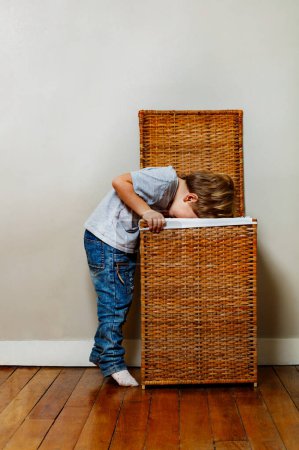Foto de Lindo niño mirar en la caja de ropa de madera doblando sobre borde vista de perfil - Imagen libre de derechos