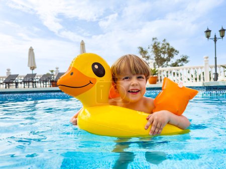 Foto de Niño nadando en una boya de pato disfrutando de la piscina riendo con un fondo soleado y iluminado - Imagen libre de derechos
