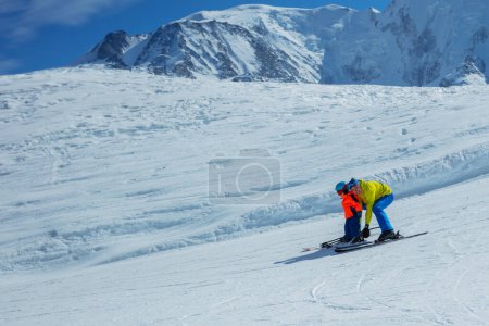 Photo for Father teaches little kid to skiing gliding behind holding ski bindings with hands showing snowplow move profile view - Royalty Free Image