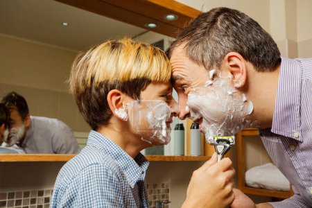 Téléchargez les photos : Père et fils avec de la mousse à raser sur le visage jouent ensemble en touchant le front, riant - en image libre de droit