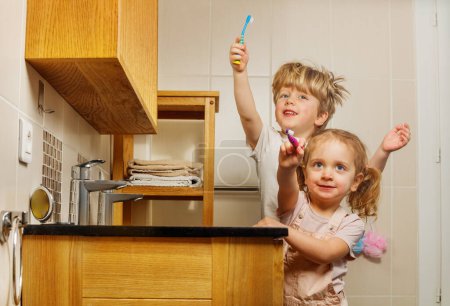 Foto de Retrato de dos niños felices hermano y hermana sosteniendo cepillo de dientes cepillarse los dientes muestran a la cámara sonriendo levantando las manos - Imagen libre de derechos