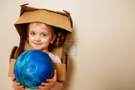 Photo for Beautiful girl in cardboard astronaut helmet hold planet earth blue green globe model in hands - close portrait - Royalty Free Image