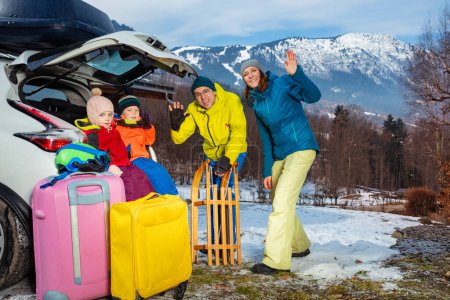 Photo for Family with mom, dad, three children standing by open car trunk arrived at alpine skiing resort unloading suitcases ski sledge and other baggage - Royalty Free Image