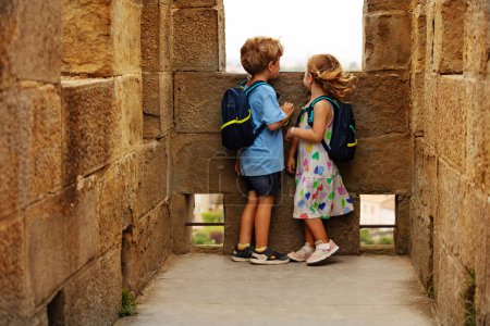 Foto de Felices turistas niño y niña con mochilas explorando las torres de piedra de Carcasona fortaleza francesa en Occitania, Francia en el día ventoso - Imagen libre de derechos