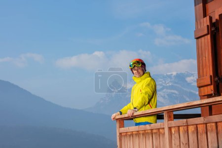 Photo for Handsome man in ski gear observe beautiful Alps from balcony of chalet, skier portrait - Royalty Free Image