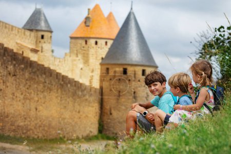 Téléchargez les photos : Petit touriste se reposant au fond des immenses fortifications de Carcassonne en Occitanie, en France, profitant de leurs vacances d'été historiques - en image libre de droit