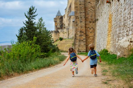 Téléchargez les photos : Les enfants font du tourisme le long des immenses murs de la ville fortifiée française de Carcassonne en Occitanie, dans le sud de la France - en image libre de droit