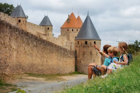Foto de Tres niños de vacaciones apuntando a las torres, descansando cerca de las murallas de la famosa ciudad fortificada de Carcasona en Occitania, Francia - Imagen libre de derechos