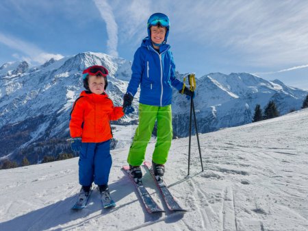 Téléchargez les photos : Grand frère skieur lien avec petit frère lui apprendre à monter sur une pente ensoleillée dans les montagnes françaises - en image libre de droit