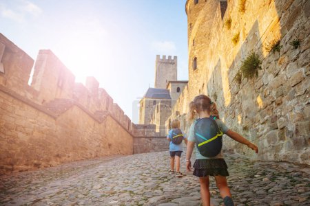 Foto de Dos niños pequeños con mochilas que se divierten corriendo dentro de la fortaleza de Carcassonne en las luces de verano del atardecer - Imagen libre de derechos
