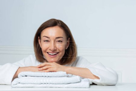 Foto de Retrato de belleza de una mujer de mediana edad riendo con una sonrisa confiada en la casita posando en el baño descansando sobre una toalla - Imagen libre de derechos